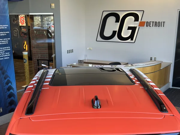 An orange-wrapped vehicle inside CG Detroit’s showroom, beneath the CG Detroit wall sign
