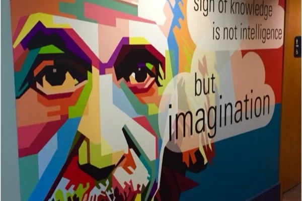 A color-block portrait mural carrying the line the true sign of knowledge is not intelligence but imagination