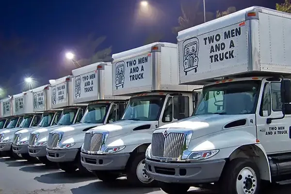 A row of TWO MEN AND A TRUCK box trucks parked at night, each carrying the same brand graphics.