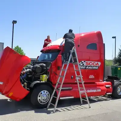 Expert installers stand on ladders applying a custom vehicle wrap to the roof of a semi truck
